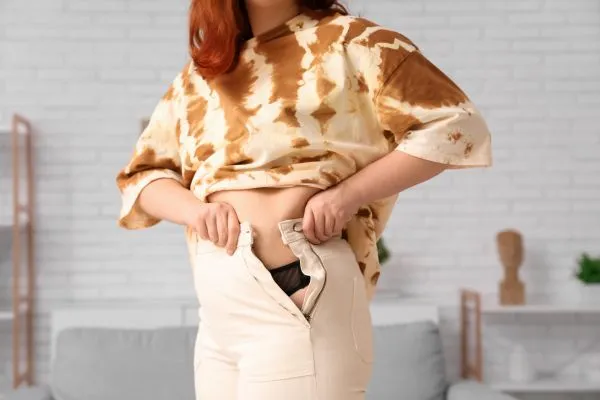 Image of woman trying to do her trousers up after pregnancy weight gain Crawley