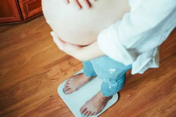 Image of woman weighing herself and experiencing weight gain through pregnancy Crawley